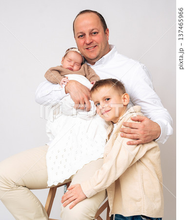 Young father holding a newborn baby while standing with his son. Warm family portrait illustrating parenting, family love and connection between siblings. Concept of fatherhood and happy childhood.  137465966