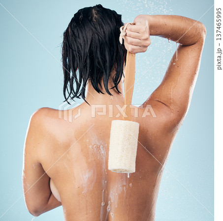 Shower, back and woman with loofah in studio for body care, wellness and cleaning on blue background. Hygiene, skincare and behind female model with scrub in a bathroom for cosmetic treatment or wash 137465995