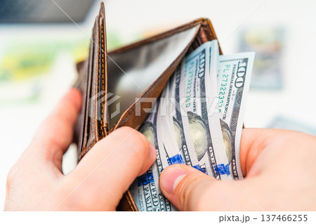 Man placing dollar banknotes into leather wallet. Cash payment, salary income, savings and financial planning concept. 137466255