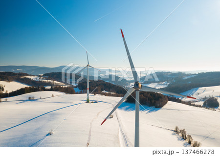 A modern wind turbine operates in an open field during winter, surrounded by snow and cold weather. A modern wind turbine operates in an open field during winter, surrounded by snow and cold weather. 137466278