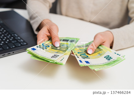 Female managing finances, counting cash and recording expenses on laptop. Savings, income tracking, and financial literacy. 137466284