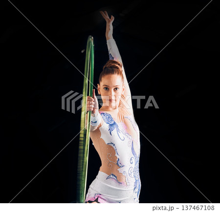 Portrait, dance with a gymnastics hoop and a woman in the gym for a performance showcase or practice. Fitness, training and concert with a female athlete on a dark background for routine or recital Portrait, dance with a gymnastics hoop and a woman in the gym for a performance showcase or practice. Fitness, training and concert with a female athlete on a dark background for routine or recital 137467108