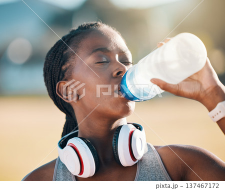 Black woman, drinking water and health, fitness and runner outdoor with headphones, thirsty after workout with cardio. Bottle, hydration and h2o, exercise and wellness with athlete, music and sports Black woman, drinking water and health, fitness and runner outdoor with headphones, thirsty after workout with cardio. Bottle, hydration and h2o, exercise and wellness with athlete, music and sports 137467172