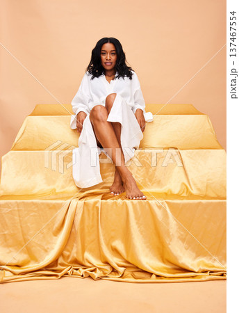 Goddess, happy and portrait of a woman on a studio background for skincare or gold aesthetic. Smile, throne and a model or girl in a robe for wellness, beauty or cosmetics while sitting on a backdrop 137467554