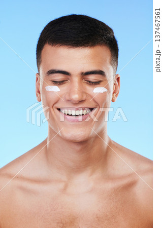 Man, beauty and face with lotion on skin, moisturizer and grooming for hygiene isolated on blue background. Sunscreen, cream and dermatology, skincare and treatment with cosmetics product in a studio Man, beauty and face with lotion on skin, moisturizer and grooming for hygiene isolated on blue background. Sunscreen, cream and dermatology, skincare and treatment with cosmetics product in a studio 137467561