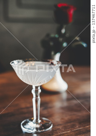 Elegant gin cocktail in a vintage coupe glass on a wooden table. Moody atmospheric lighting with soft bokeh and film grain. Ideal for luxury bar menus, romantic themes, and celebration designs. 137467711