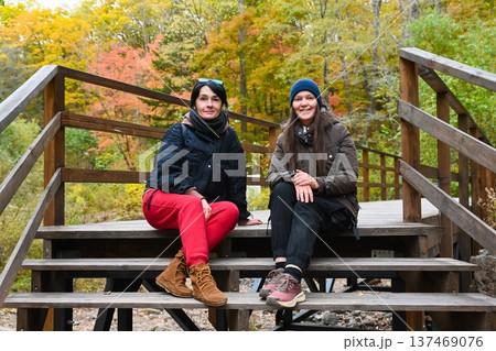 Two Russian women travelers friends sitting on wooden stairs in autumn forest Russia one 50 years old and one 35 years old enjoying nature journey Two Russian women travelers friends sitting on wooden stairs in autumn forest Russia one 50 years old and one 35 years old enjoying nature journey 137469076