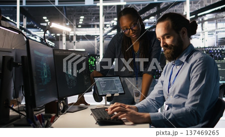 Data center system administrators working together, collaborating on neural network software development. Server hub worker and african american colleague implementing AI tech in workplace, camera A Data center system administrators working together, collaborating on neural network software development. Server hub worker and african american colleague implementing AI tech in workplace, camera A 137469265