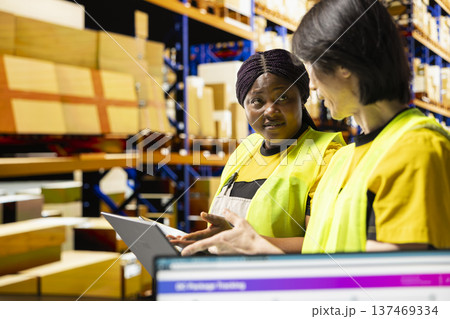 Diverse employees oversee the packaging and shipping of e-commerce goods in a modern large scale logistics center. Workers organize inventory and prepare parcels for immediate dispatch. 137469334