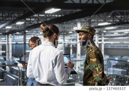 Soldier in server room uses geospatial data to support evacuation during emergency operations. Military data center personnel in uniform coordinating disaster response logistics control. 137469337