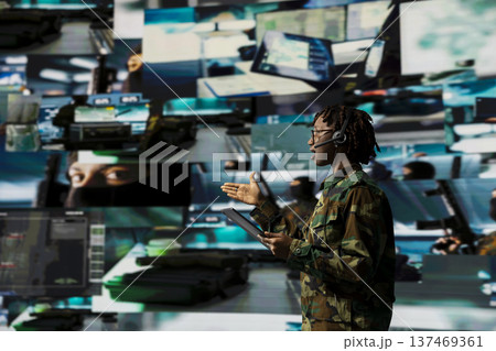 Army telecommunications dispatcher uses tablet and headset microphone to speak with units on combat field. Soldier in command center manages encrypted communication channels Army telecommunications dispatcher uses tablet and headset microphone to speak with units on combat field. Soldier in command center manages encrypted communication channels 137469361