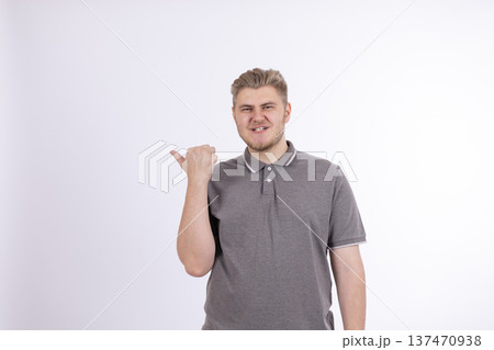 Man in gray t-shirt pointing thumb to the side 137470938