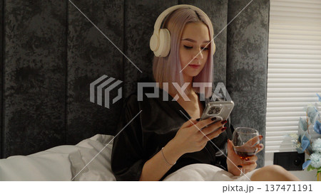 Girl in bed with headphones using her smartphone Girl in bed with headphones using her smartphone 137471191