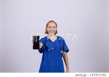 Female nurse holding smartphone and looking at camera Female nurse holding smartphone and looking at camera 137471192