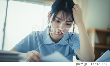 介護施設で書類を前に疲れ果て、悩み考え込む若い女性介護士。労働問題やメンタルケアのイメージ 137471665