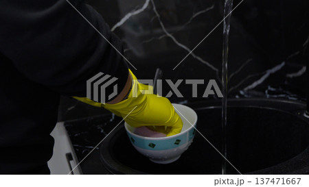 Hand in yellow glove washing dishes under running water 137471667