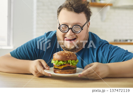 Overweight man at home admiring a juicy burger in kitchen, dieting temptation 137472119