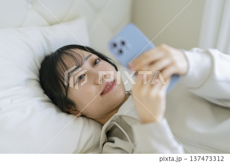 寝転んでスマートフォンの画面を見つめる若い女性 寝転んでスマートフォンの画面を見つめる若い女性 137473312