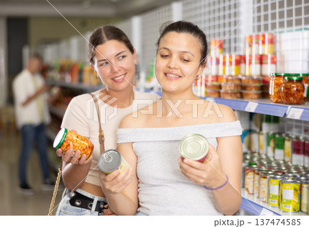 Two female shoppers choosing canned food in grocery store 137474585