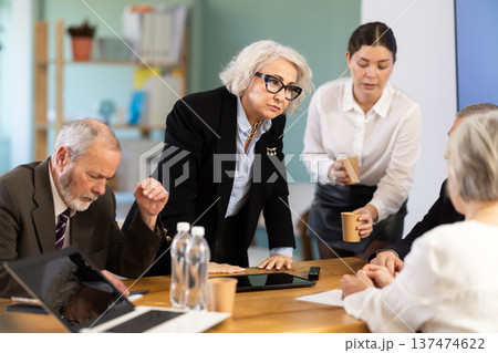 Elderly woman standing and scolding sad senior colleagues at meeting table Elderly woman standing and scolding sad senior colleagues at meeting table 137474622