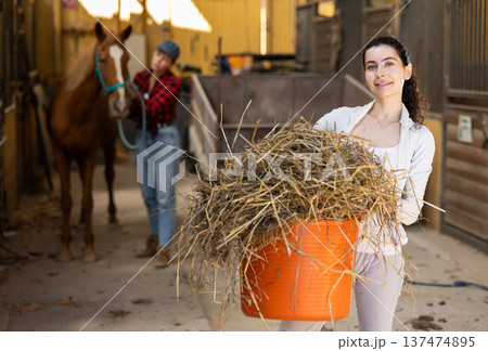 Young woman with bucket of hay in stable 137474895