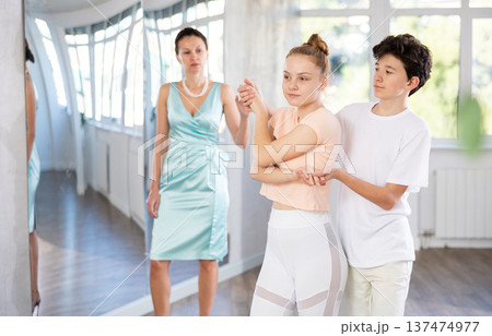 Experienced dance teacher teaching ballroom dancing to a couple of teenagers in studio 137474977