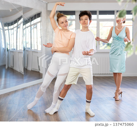 Experienced dance teacher teaching ballroom dancing to a couple of teenagers in studio 137475060