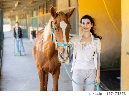 Young woman leads horse out of stable 137475278