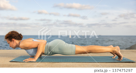 Yoga practice on embankment, female athlete fulfil carry out Chaturanga dandasana 137475297