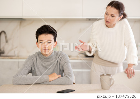 Portrait of offended boy sitting at home while mother berating him Portrait of offended boy sitting at home while mother berating him 137475326