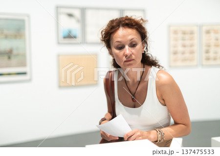 Thoughtful woman examining photographs on walls in art gallery 137475533