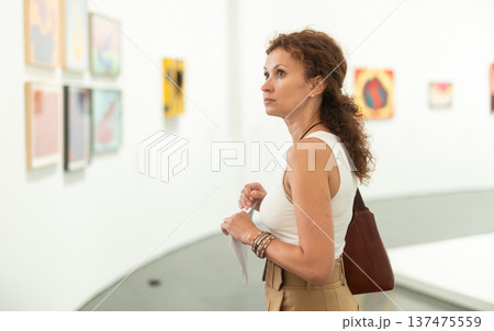Middle-aged woman looking at pictures on wall in museum Middle-aged woman looking at pictures on wall in museum 137475559