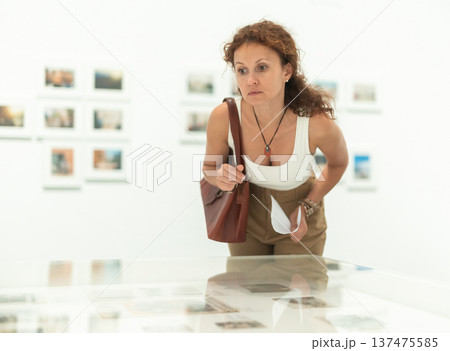 Middle-aged woman looking at objects under showcase in museum 137475585