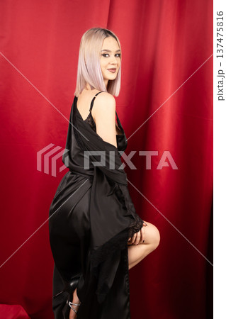 Mysterious woman in black silk robe posing against red curtain 137475816