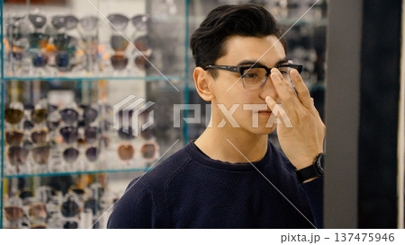 Man adjusting eyewear frame while looking at mirror in shop 137475946