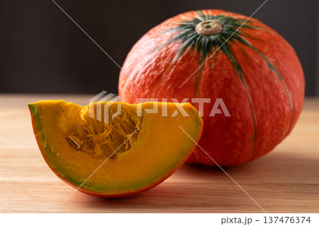 Sliced orange Kuri squash (Hokkaido pumpkin) on a wooden background, preparing for cooking Sliced orange Kuri squash (Hokkaido pumpkin) on a wooden background, preparing for cooking 137476374