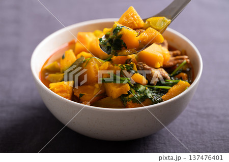 Thai spicy pumpkin curry soup with pork in a bowl scooping by spoon and eating Thai spicy pumpkin curry soup with pork in a bowl scooping by spoon and eating 137476401