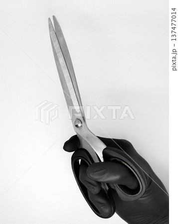 Black and white photo of a hand in a black glove holding a scissors Black and white photo of a hand in a black glove holding a scissors 137477014