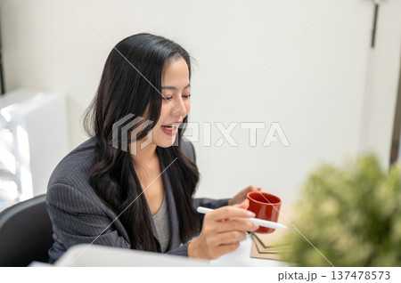 Close up businesswoman or office worker holding pen and coffee mug while looking at laptop on table. Close up businesswoman or office worker holding pen and coffee mug while looking at laptop on table. 137478573