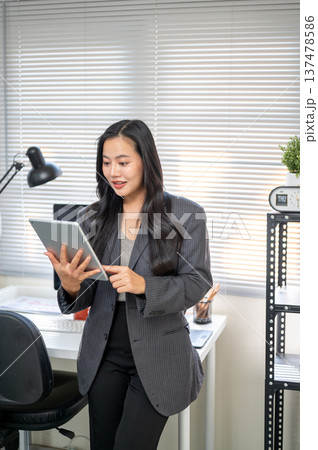 Asian businesswoman or office worker looking at tablet in surprised while standing at computer table Asian businesswoman or office worker looking at tablet in surprised while standing at computer table 137478586