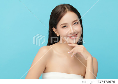 A beautiful young Asian woman with clean, fresh skin against a blue background. Skincare, facial treatment, cosmetology, beauty, and spa. An elegant portrait of an Asian woman. 137478676