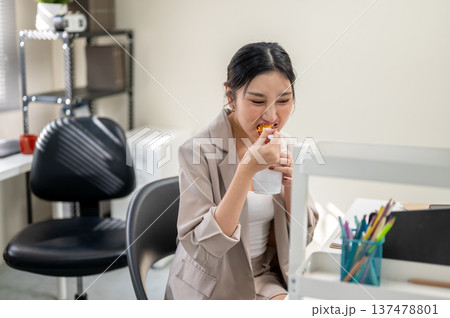 Hungry asian businesswoman or office worker enjoy eating instant noodle cup aside document on table. Hungry asian businesswoman or office worker enjoy eating instant noodle cup aside document on table. 137478801