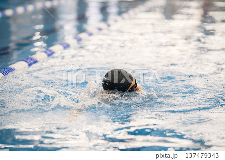 Photo of a man wearing special hat for swimming. Man swimming breaststroke in swimming pool. Professionale male swimmer training. 137479343