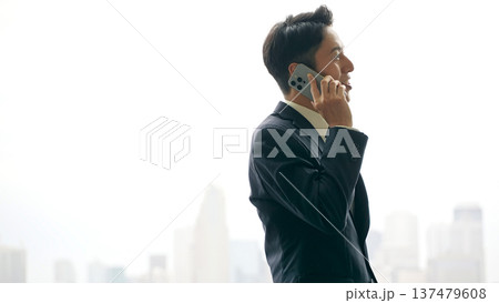 都市を背景にスマホで通話する男性ビジネスパーソン 137479608