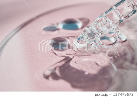Cosmetic serum pipette applying clear liquid droplets and bubbles on pink background 137479672