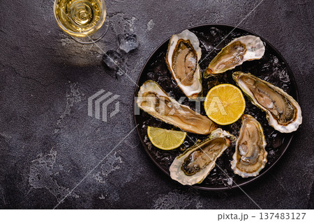 Opened fresh oysters on a plate, served with lemon and ice. Opened fresh oysters on a plate, served with lemon and ice. 137483127