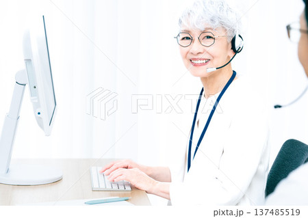 ヘッドセットをつけてパソコン操作をするシニア女性 137485519