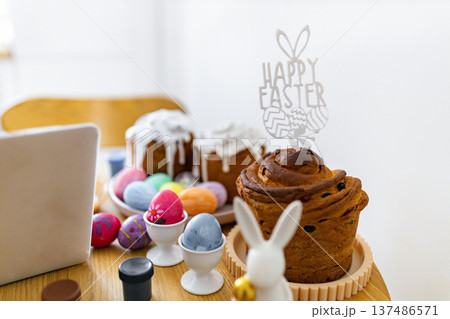 A festive table setting features traditional Easter cakes, colorful painted eggs in holders, and a 'Happy Easter' cake topper with bunny ears A festive table setting features traditional Easter cakes, colorful painted eggs in holders, and a 'Happy Easter' cake topper with bunny ears 137486571