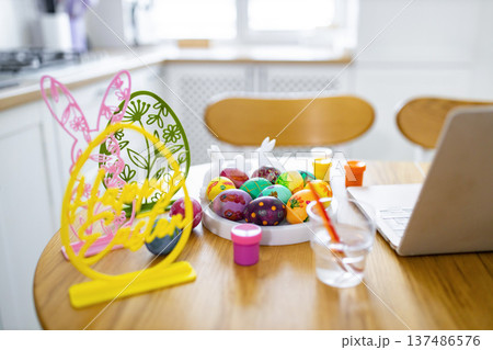 A bright kitchen table is set up for Easter egg decorating with colorful painted eggs, craft supplies, and a laptop for inspiration 137486576