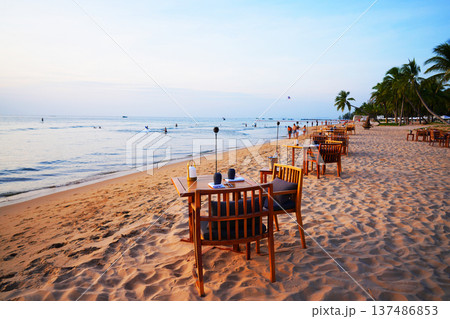 Table for dining on sand beach. People swim in ocean shoreon. Sea resort beach.  137486853